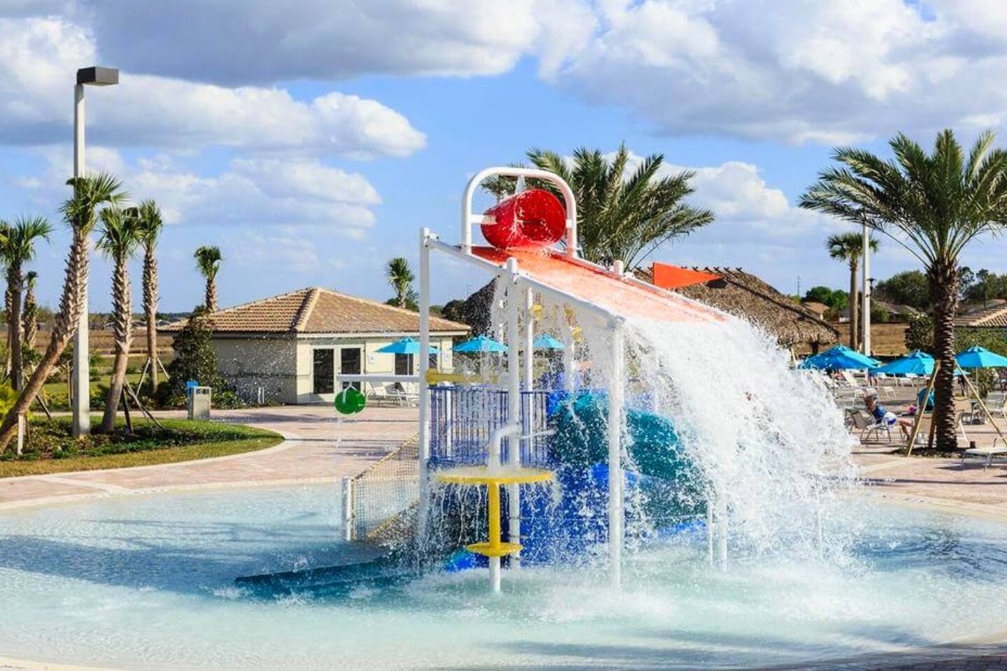 Kids' splash pad with dump bucket and slide at the resort clubhouse pool