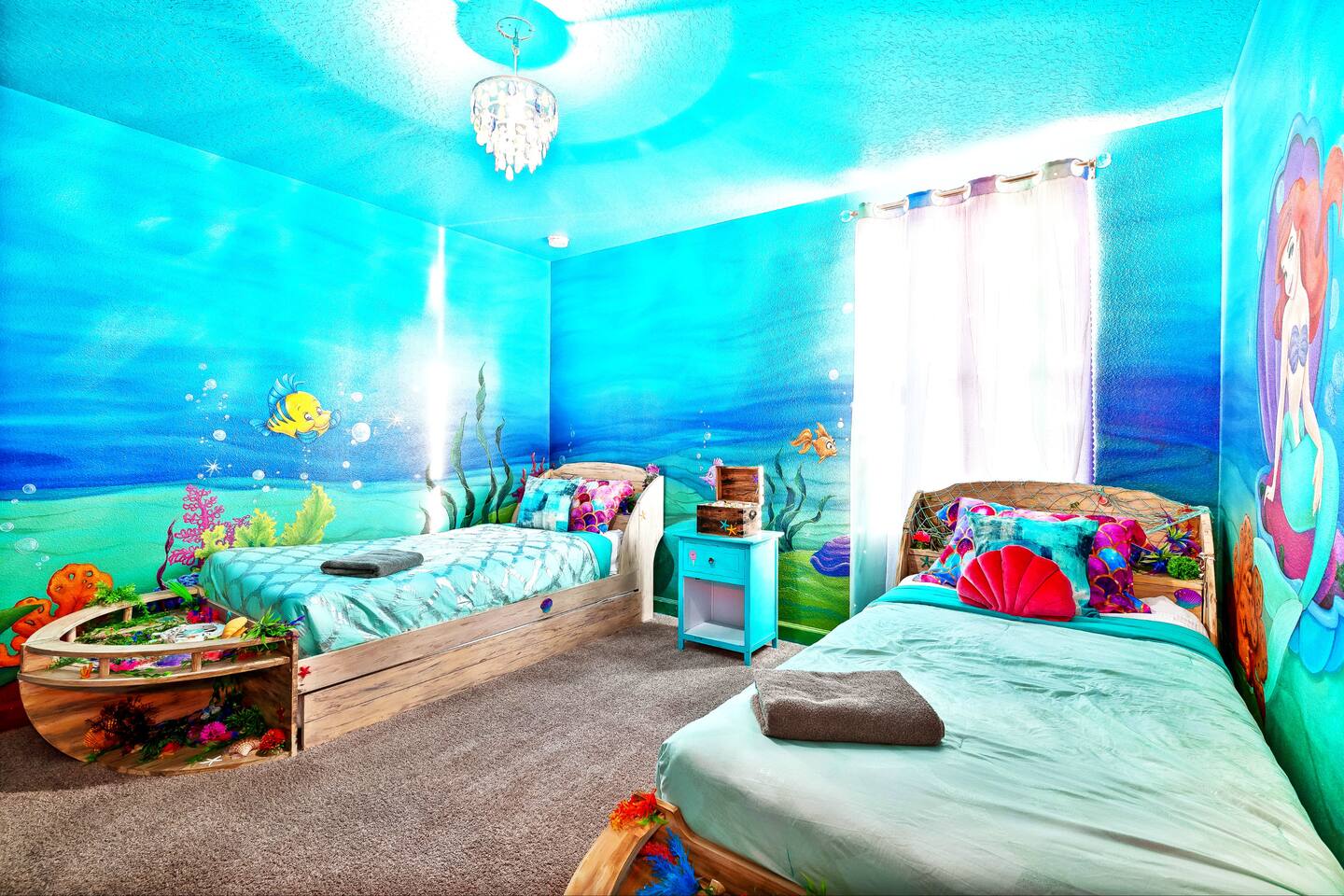 Ariel room's twin beds beneath a shell chandelier with wraparound ocean mural