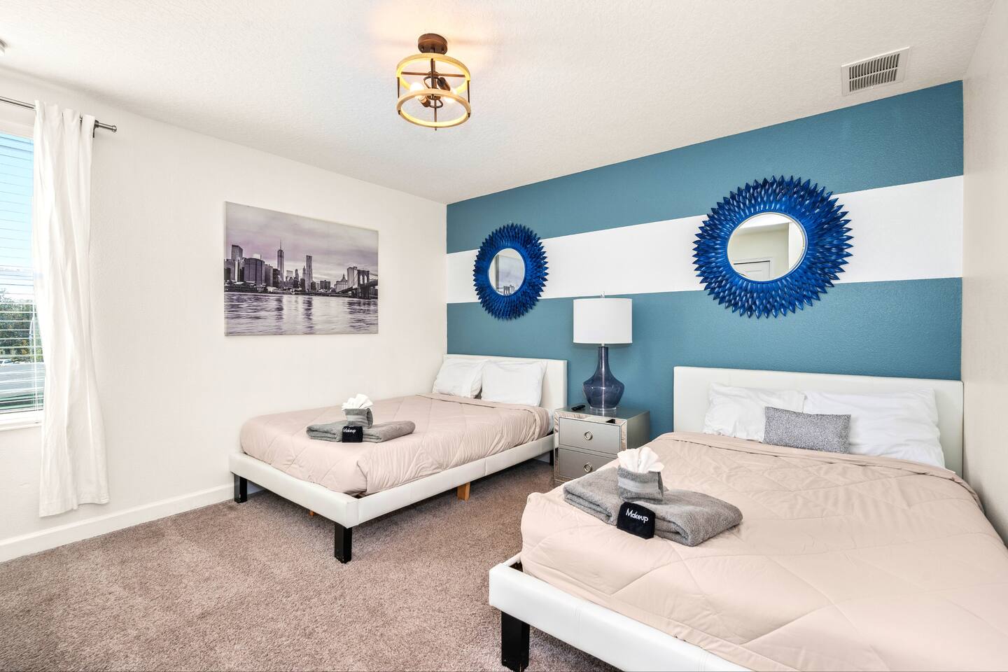 Guest bedroom with two plush beds and a navy striped accent wall with sunburst m