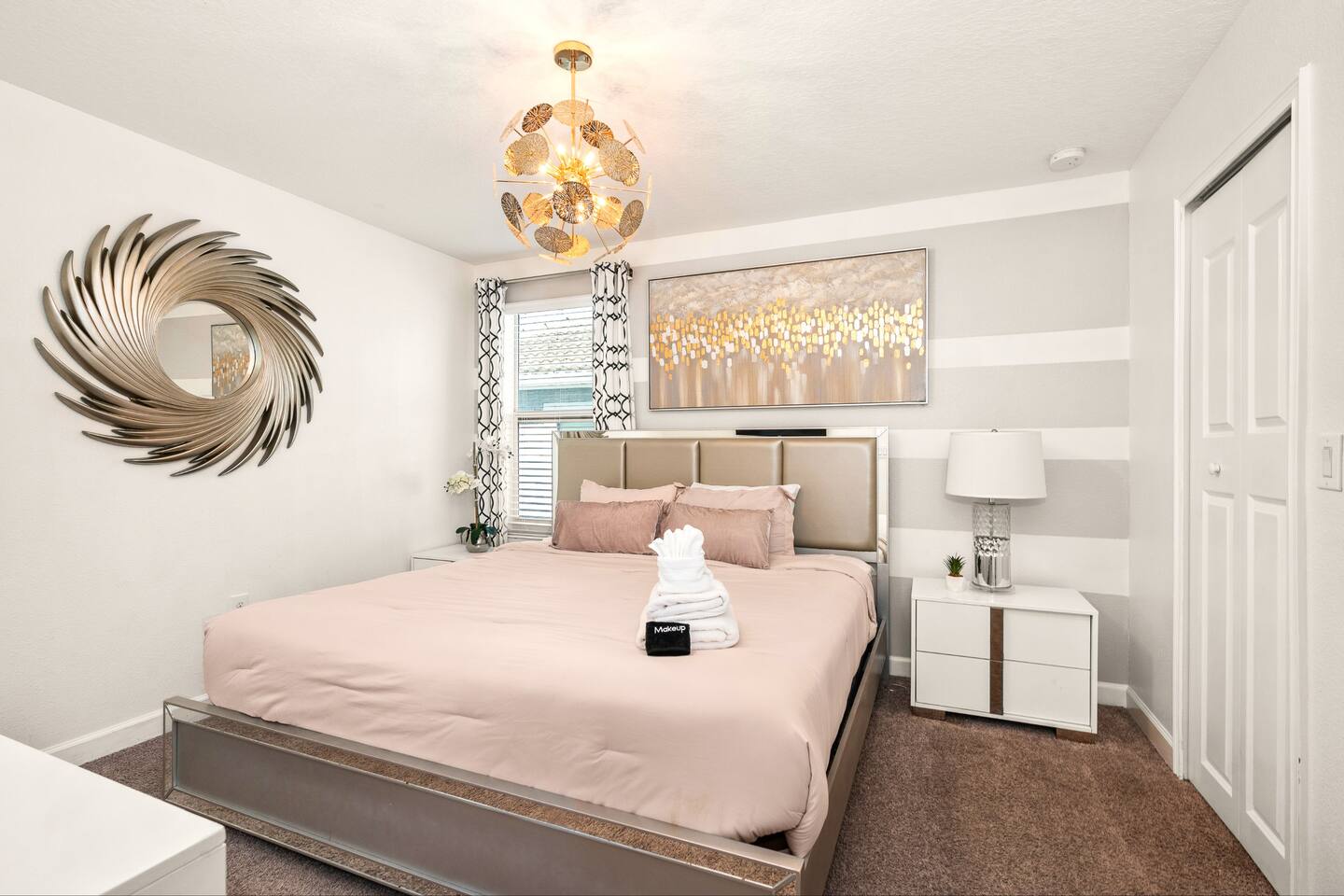 Glam bedroom with champagne upholstered king bed, gold sunburst mirror, and stri