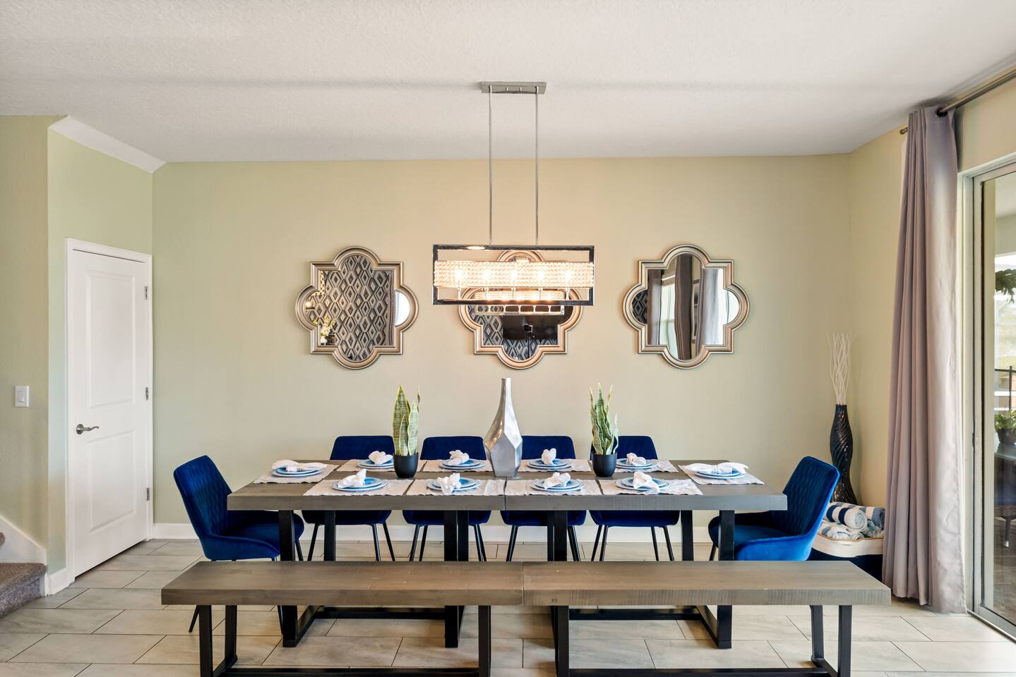 Formal dining table with velvet chairs and bench seating beneath a trio of mirro