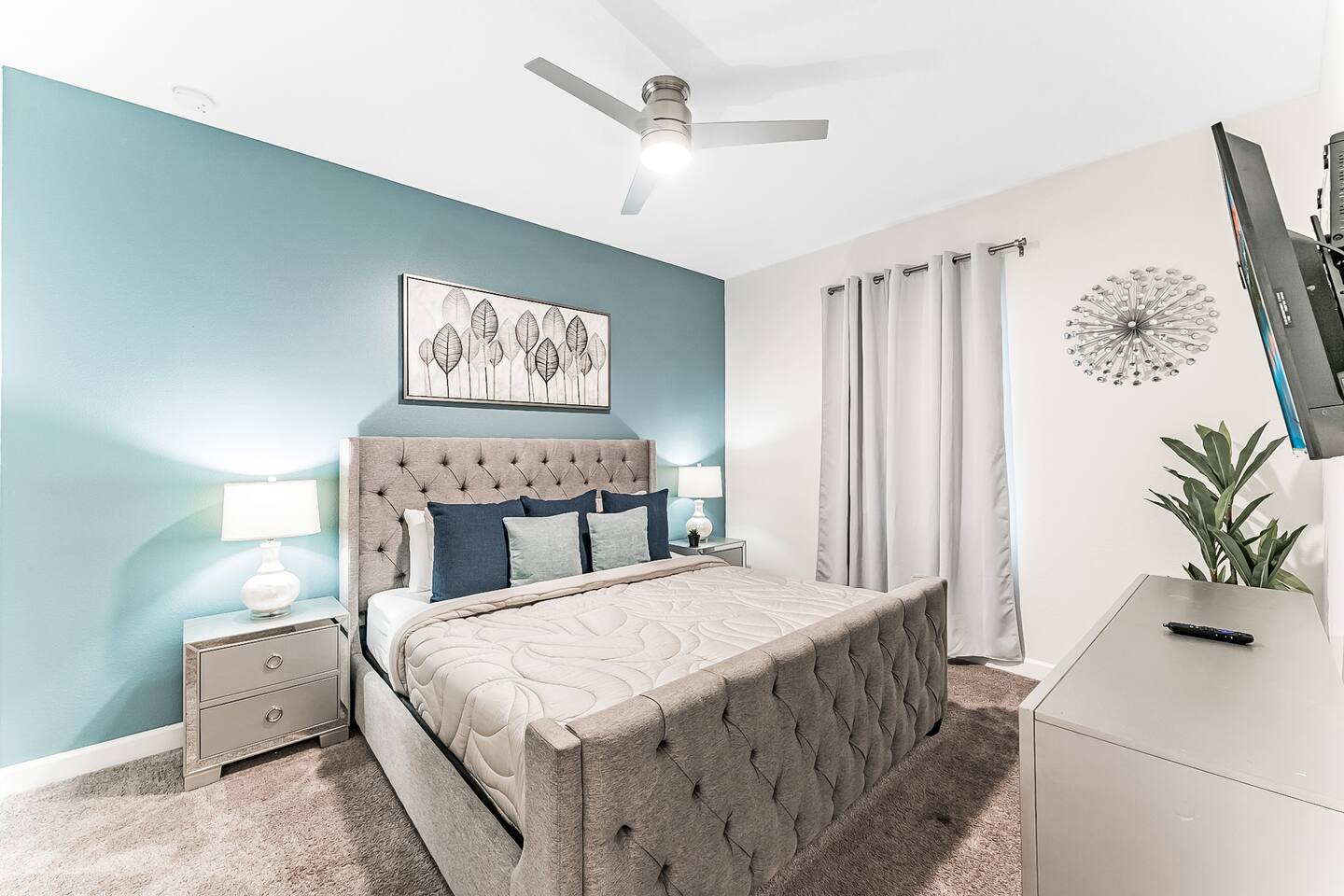King bedroom with teal accent wall, wall-mounted TV, and dresser