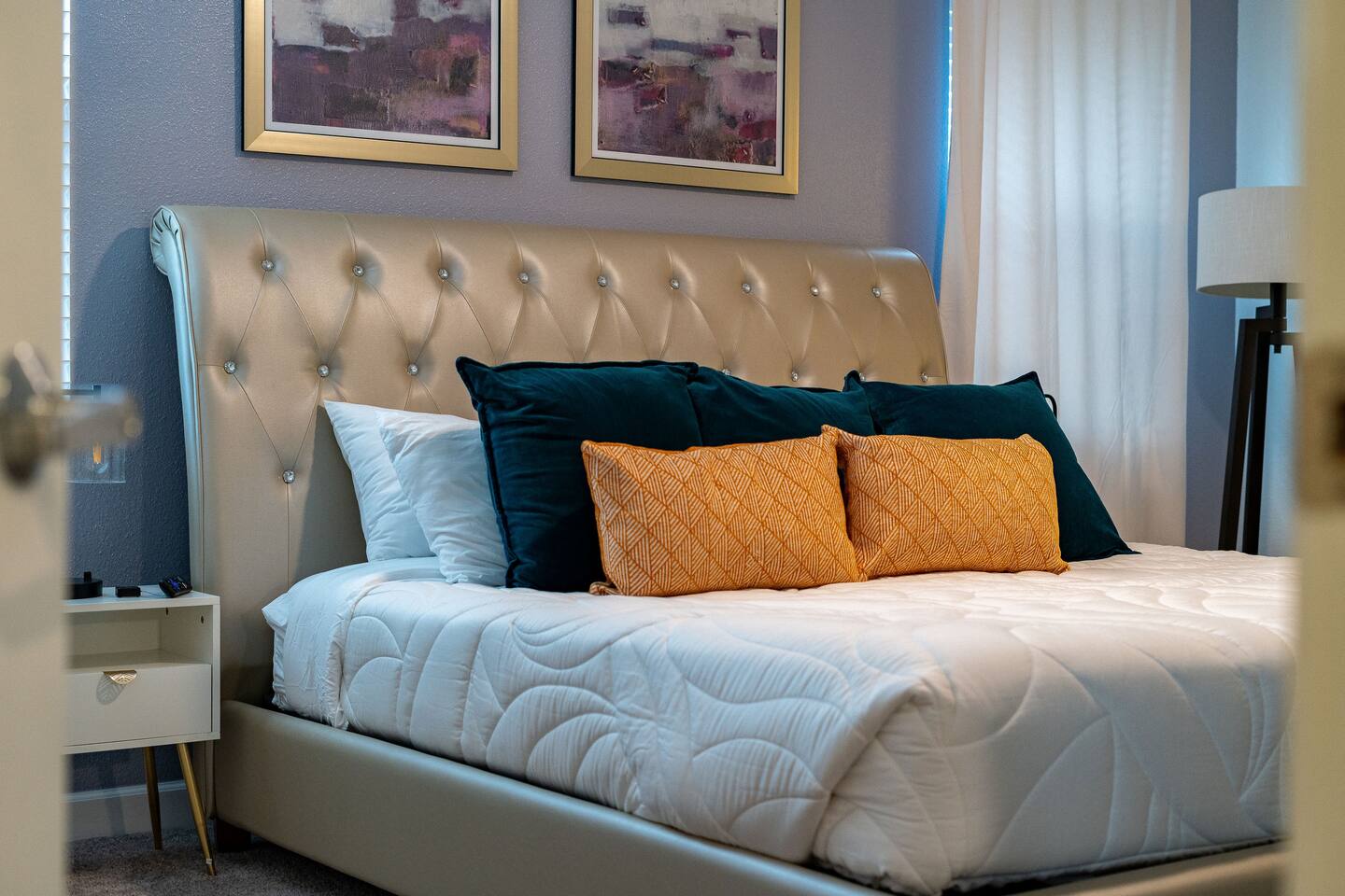 King bedroom with tufted champagne headboard and abstract artwork