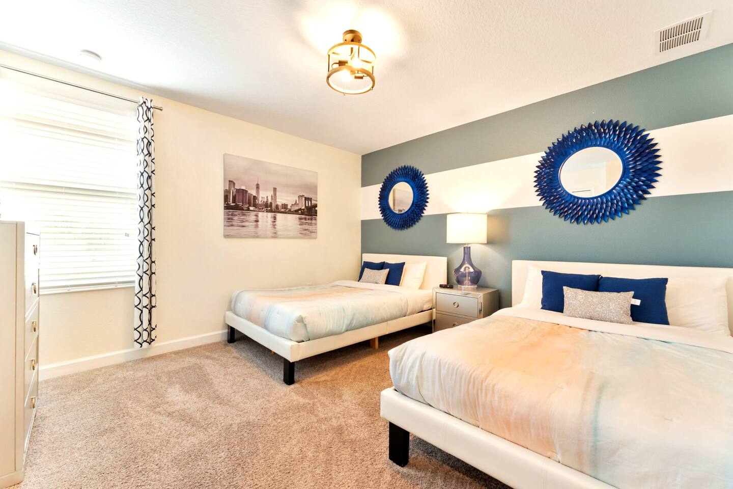 Double-queen bedroom with striped accent wall, sunburst mirrors, and city-skylin
