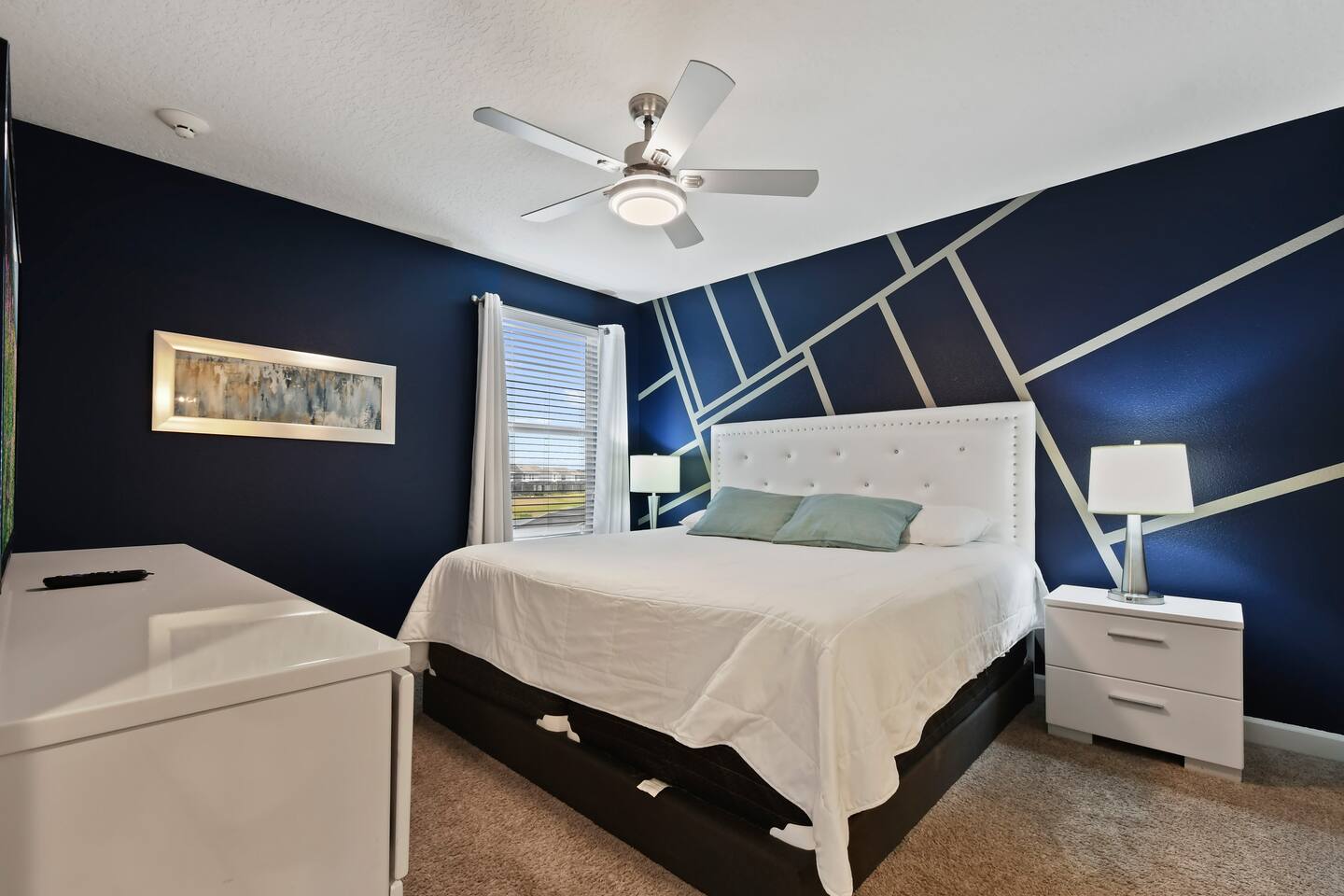 King bedroom with navy geometric accent wall and white tufted headboard