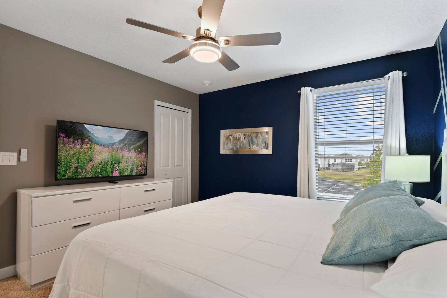 King bedroom with navy accent wall, dresser, and wall-mounted TV