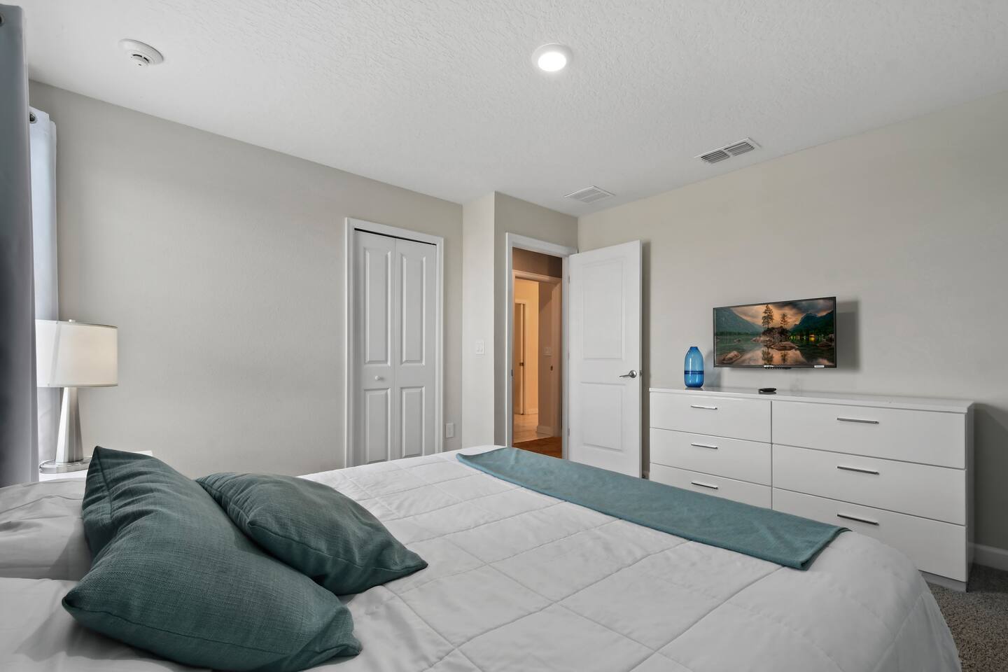 Bedroom with king bed, teal pillows, dresser, and mounted TV