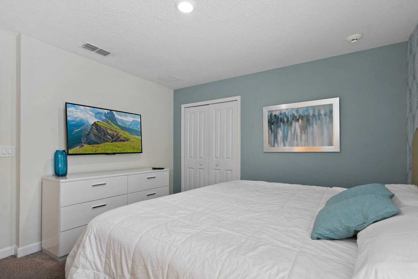 Bedroom with king bed, blue accent wall, and TV dresser