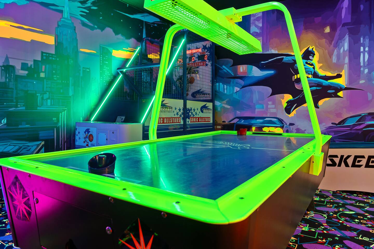Game room lineup: neon air hockey, arcade basketball, and skee ball beneath a Ba