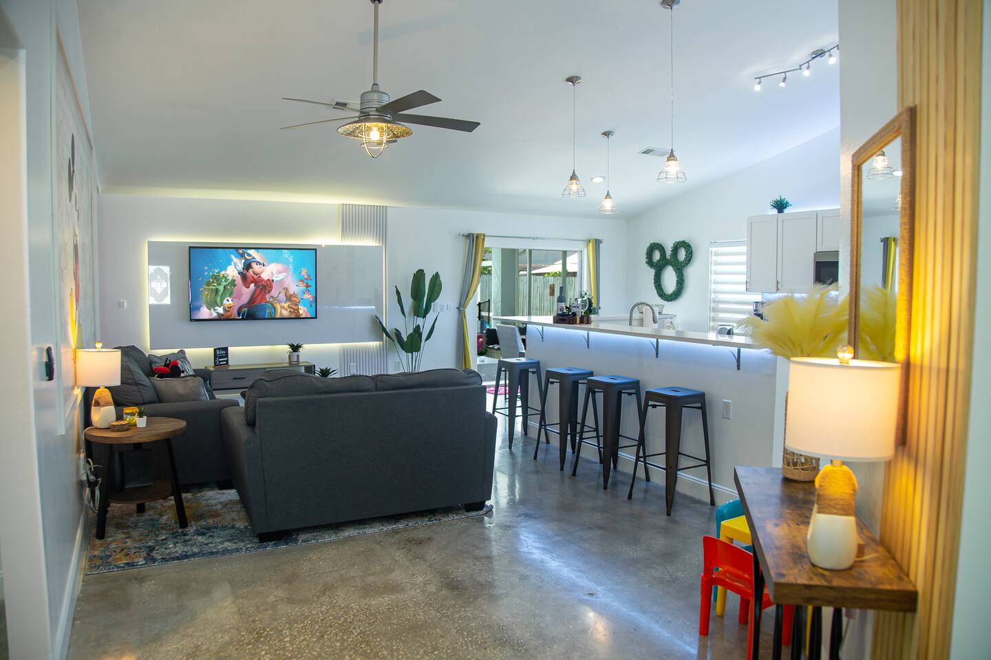 Open-plan living area with a sectional, wall-mounted TV, and kitchen breakfast b