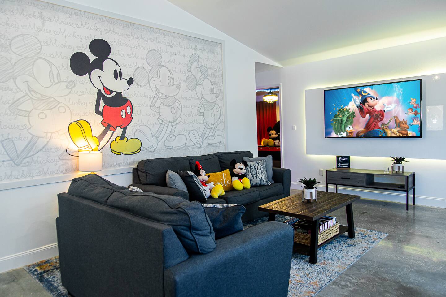 Living room with a Mickey Mouse mural, dark sectional sofas, and a mounted TV.