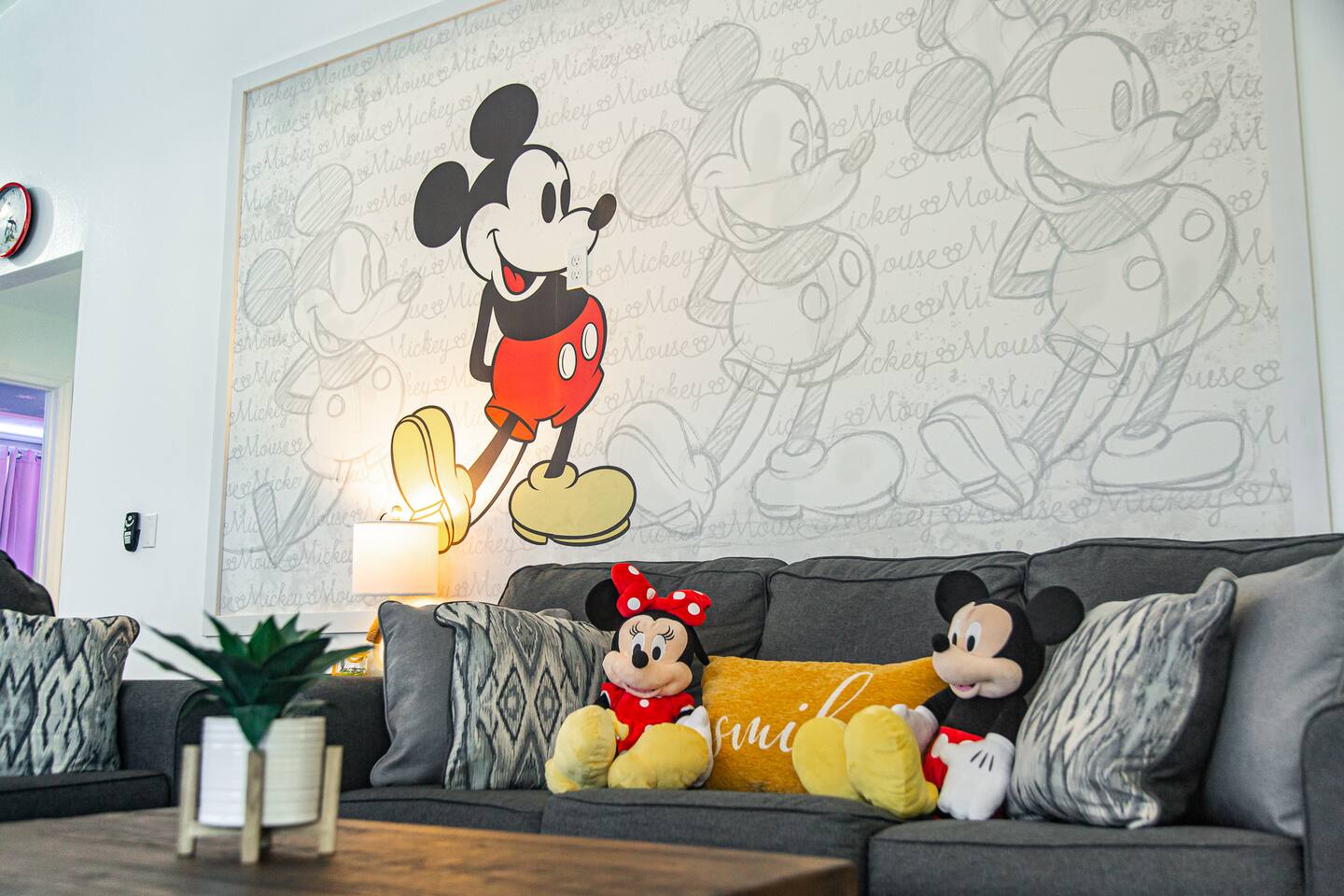 Mickey and Minnie plush toys on a sectional beneath a Mickey Mouse mural.
