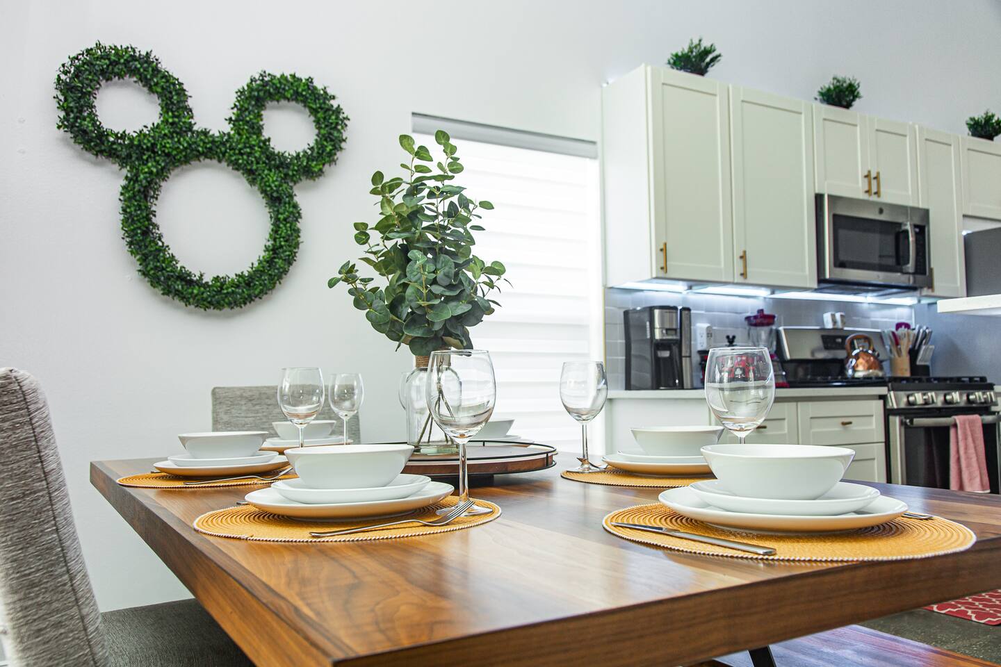 Dining table place settings beside a Mickey topiary and the kitchen.