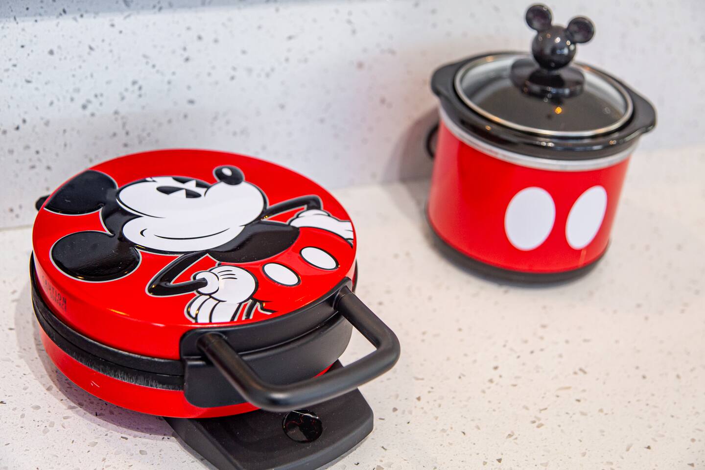 Mickey Mouse waffle maker and mini slow cooker on a countertop.