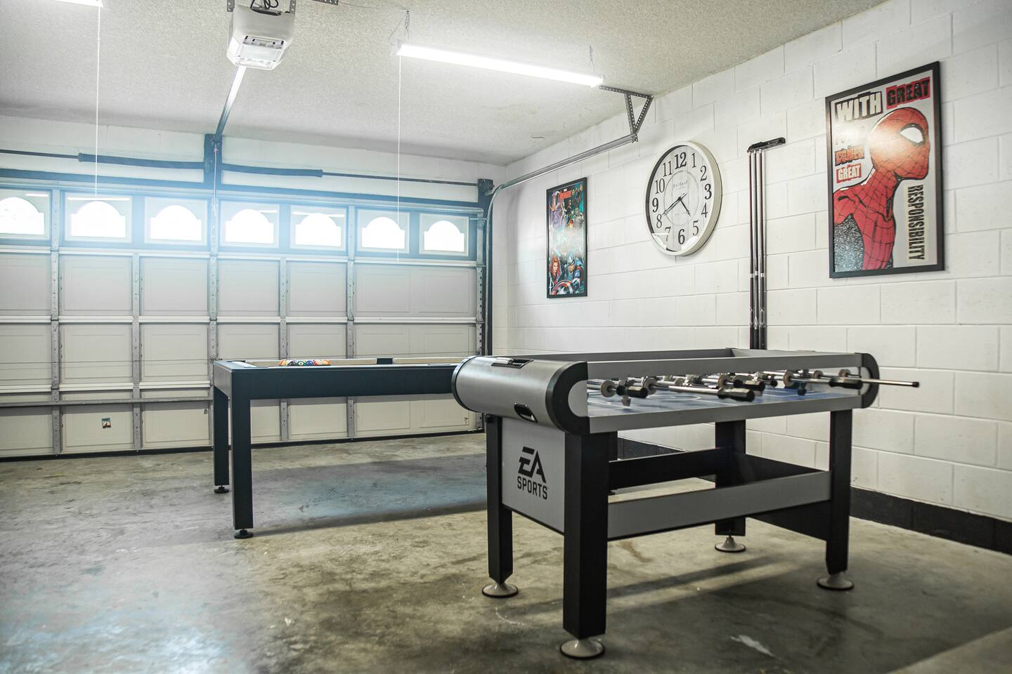 Garage game room with air hockey, a pool table, foosball, and superhero posters.