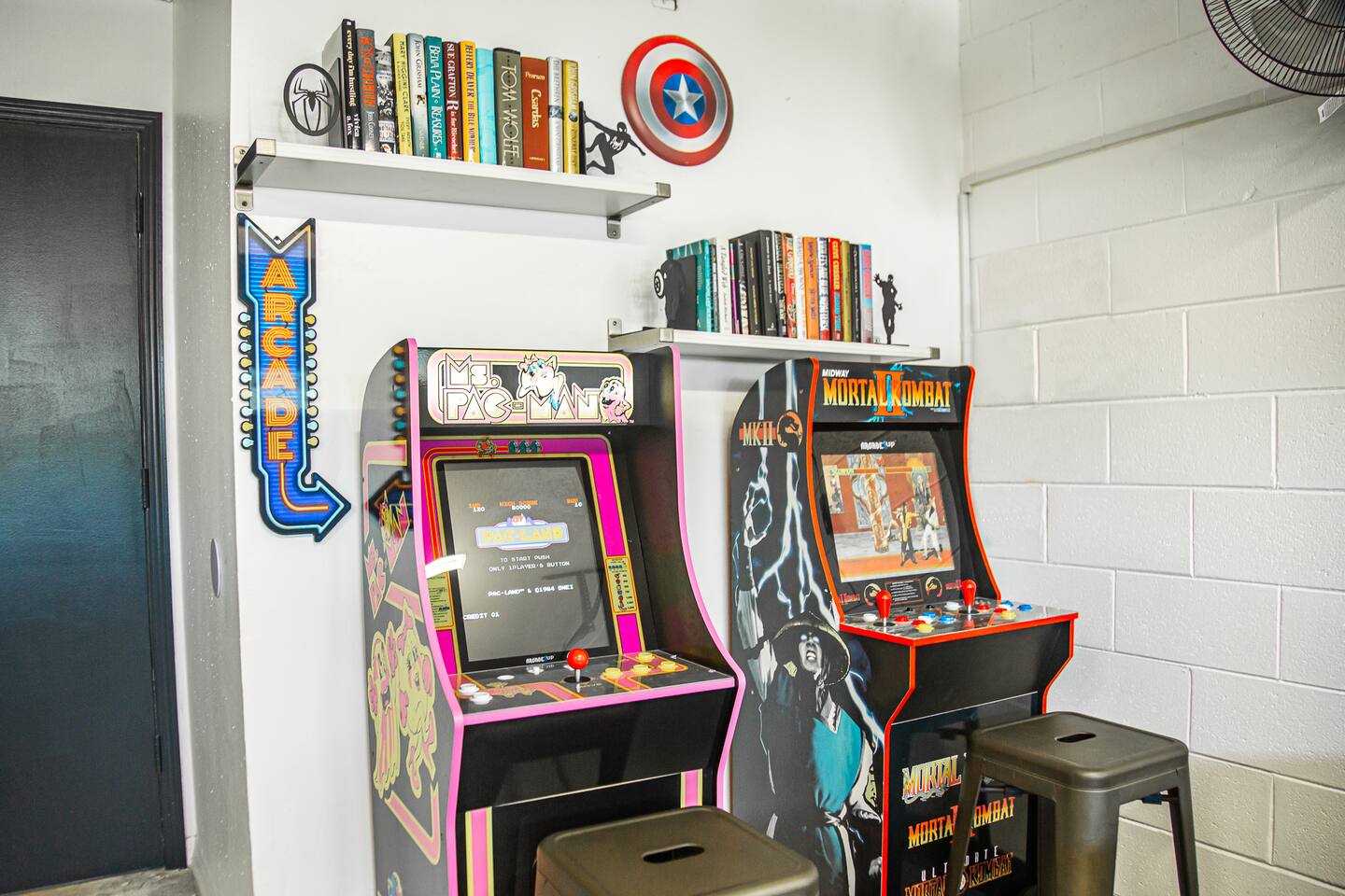 Ms. Pac-Man and Mortal Kombat arcade machines beside bookshelves.
