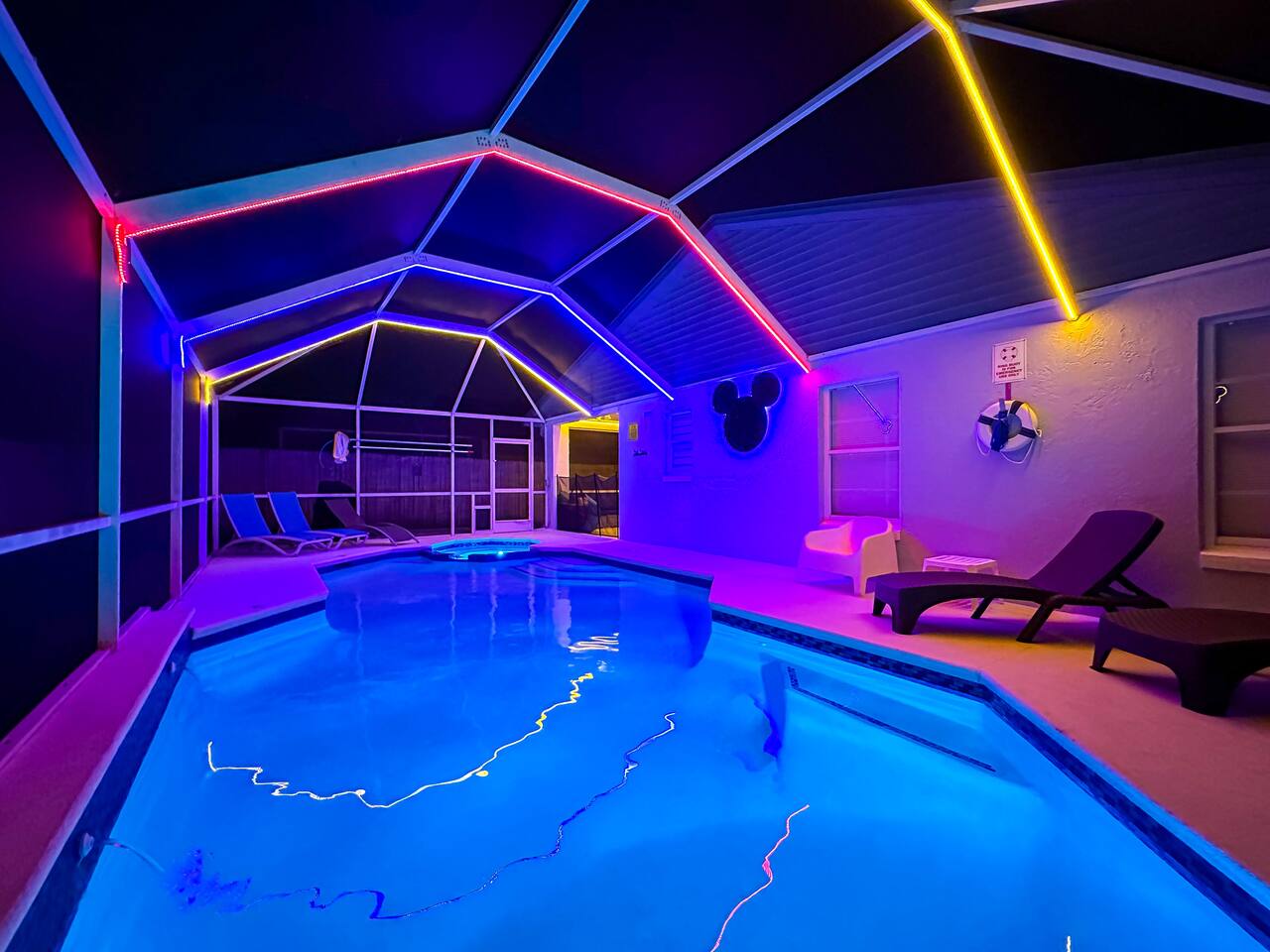 Screened pool and spa illuminated by rainbow LED lighting at night.