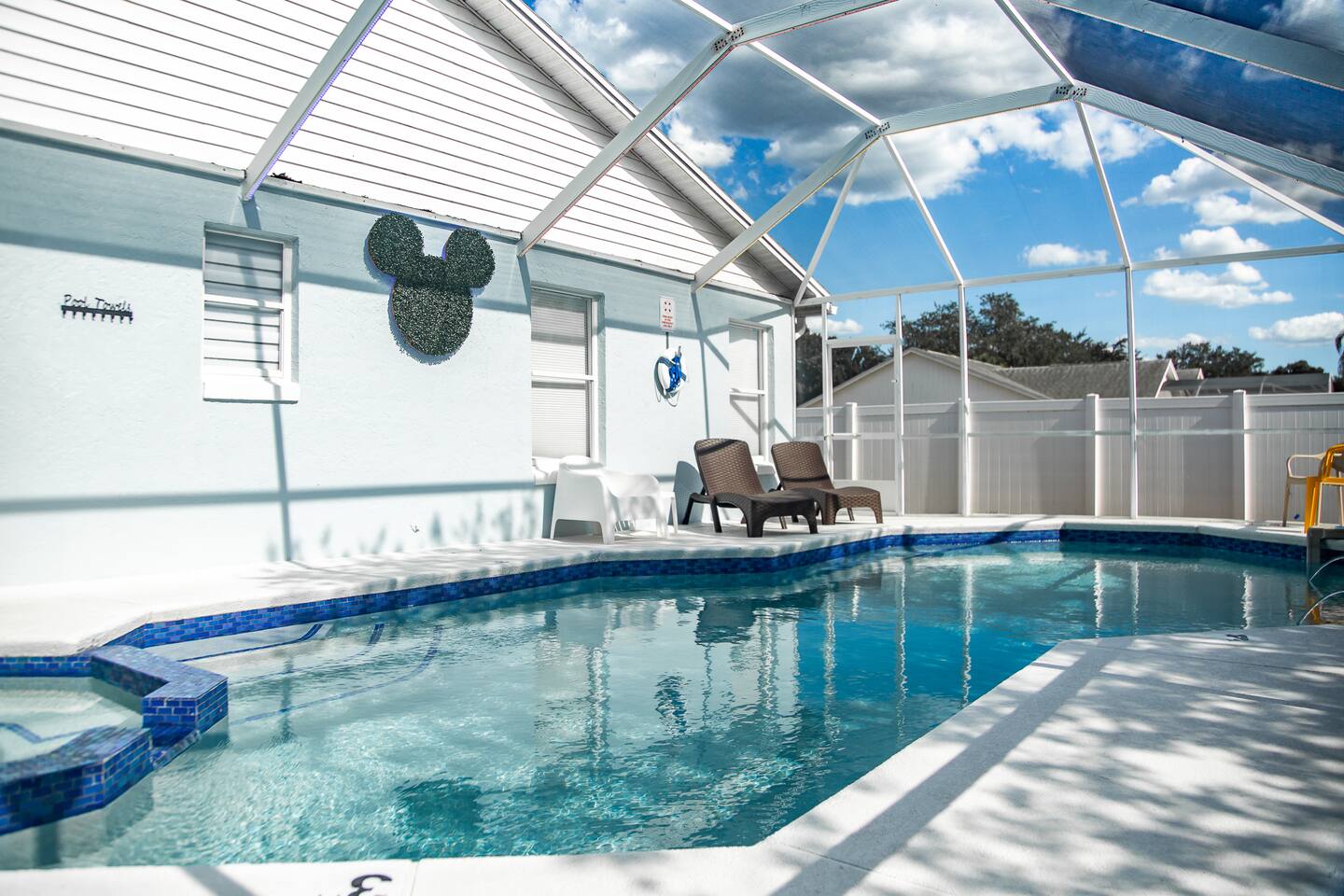 Daytime screened pool and spa with a Mickey topiary on the wall.