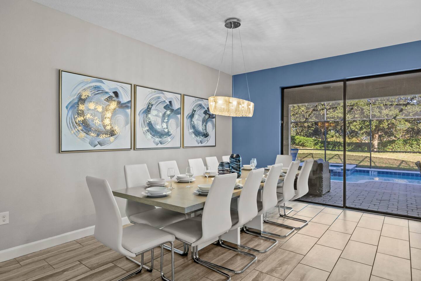Dining room with a table set for twelve beneath a chandelier, next to sliders ov