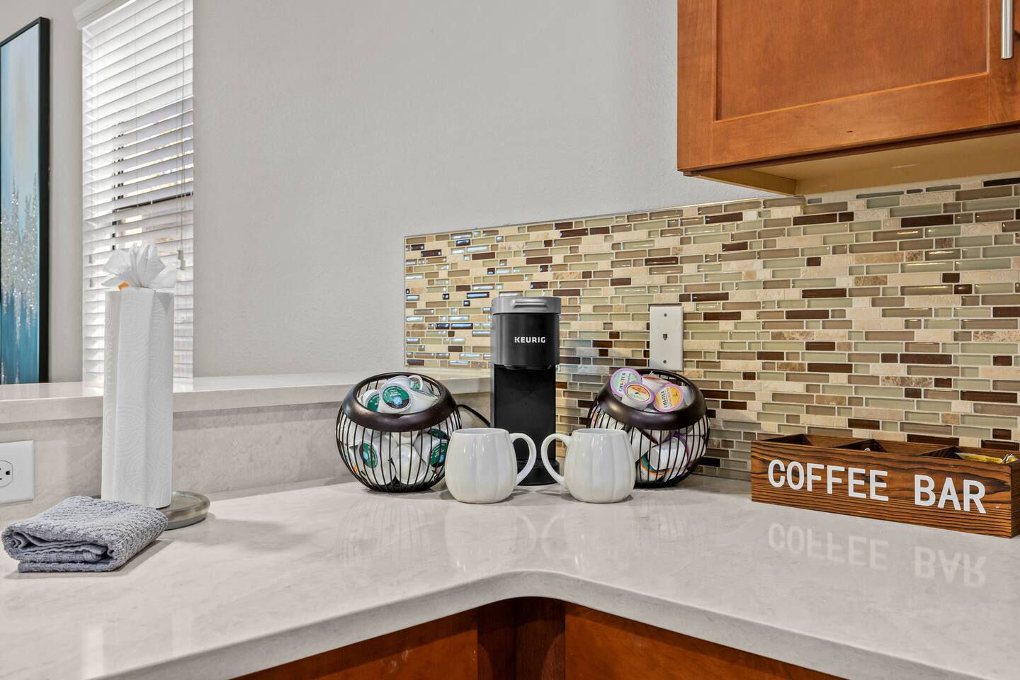 Coffee-bar corner with Keurig brewer, pod baskets, mugs, and a wooden Coffee Bar