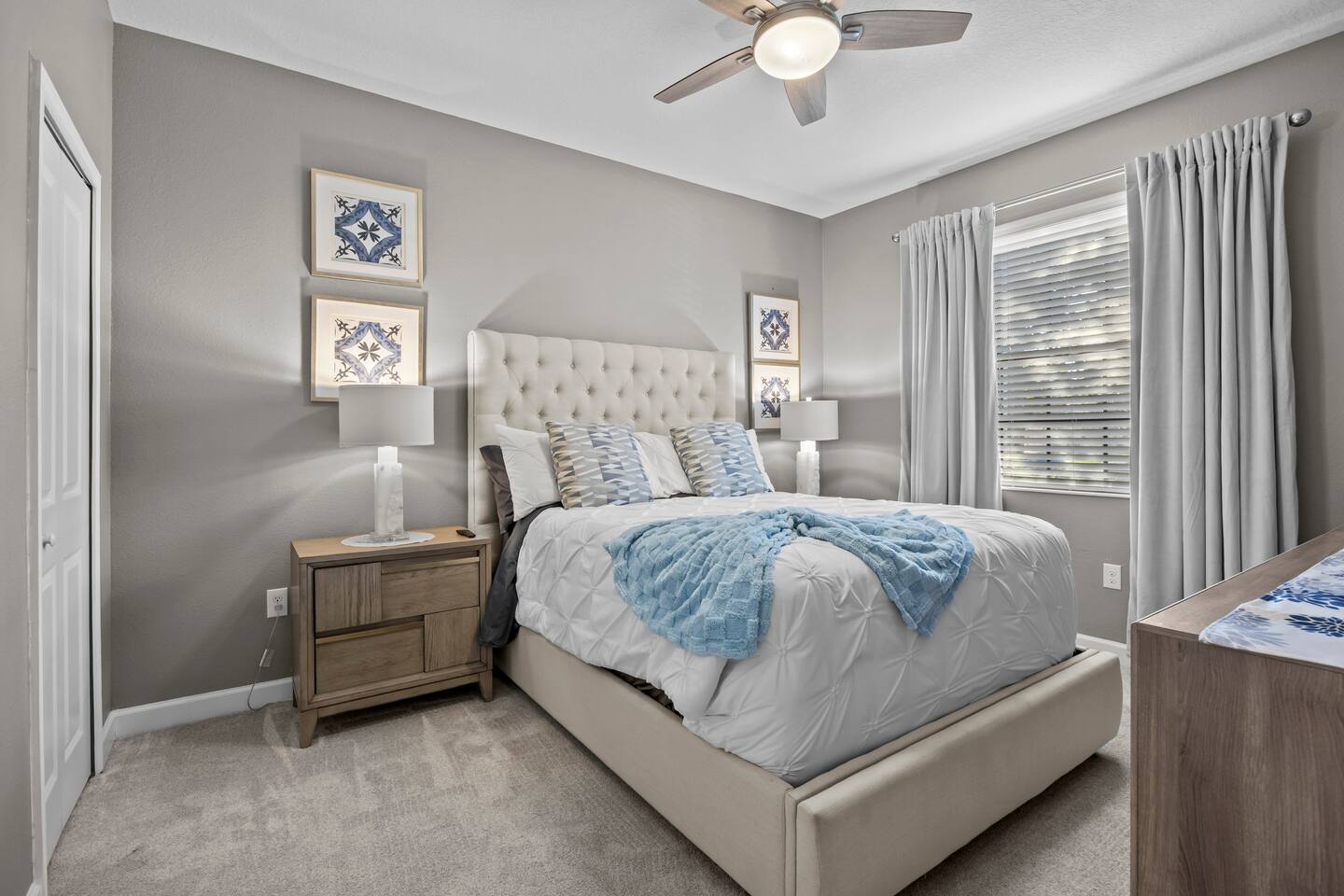 Bedroom with tufted cream headboard, white pinch-pleat bedding, and blue accent 