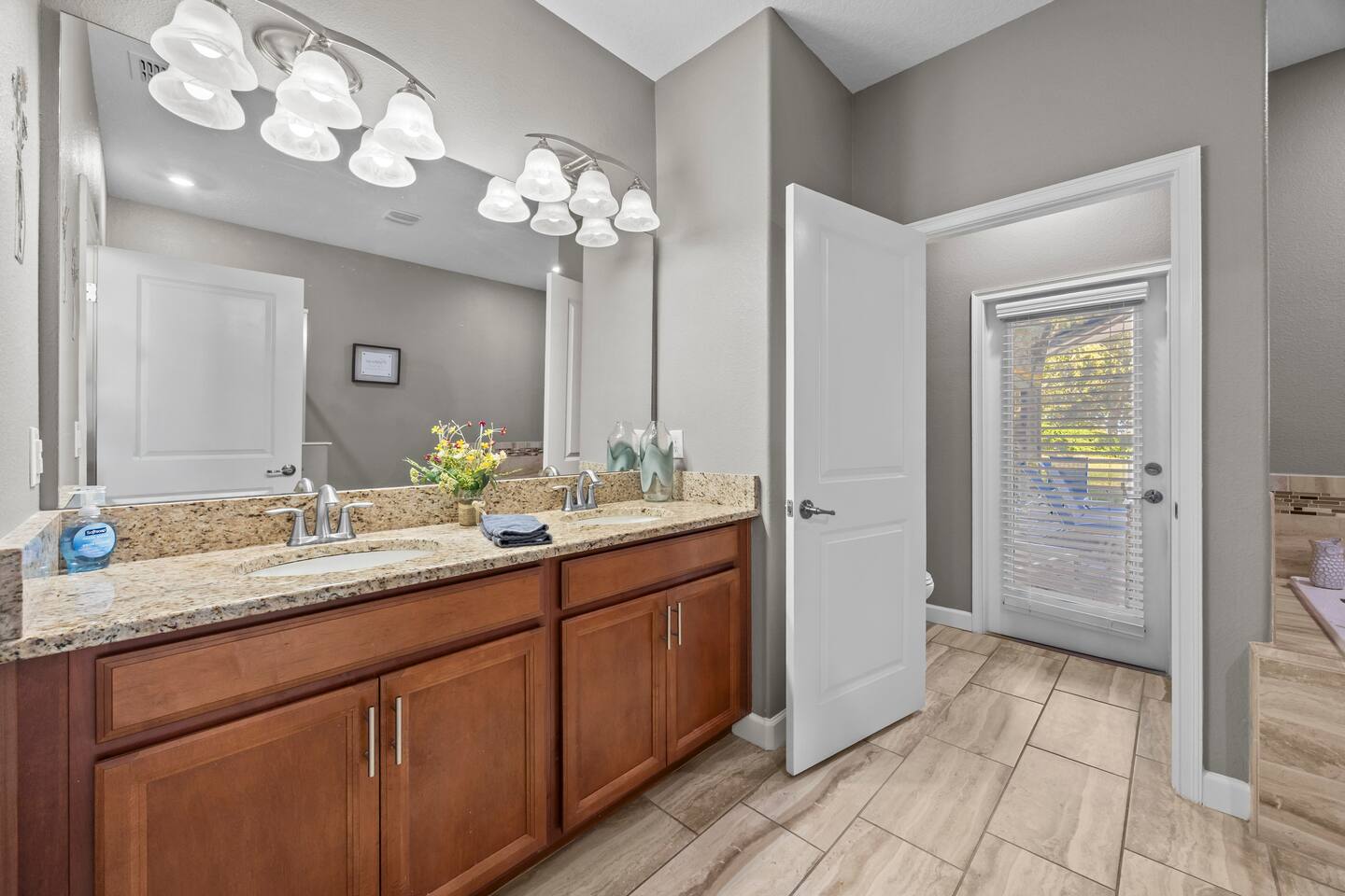 Primary bathroom with long double vanity and a glass door leading toward the poo