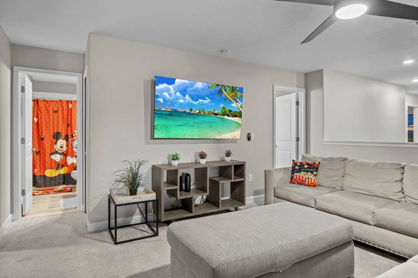 Movie loft with wall TV, cube-shelf console, and a peek into the Mickey-themed h