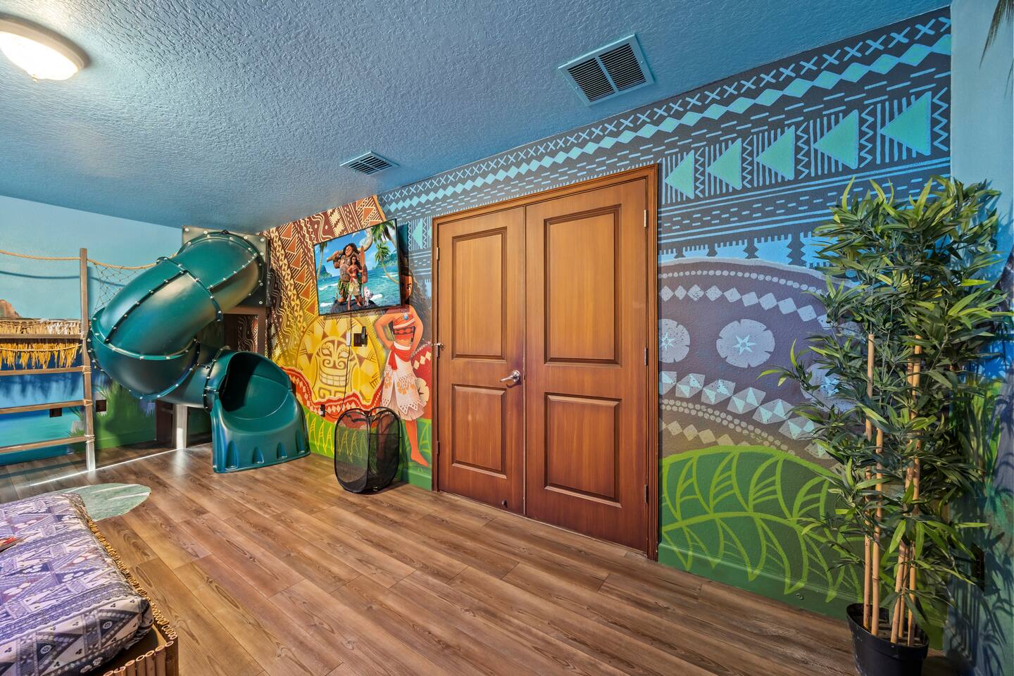 Moana suite entry wall with tribal-pattern mural, wall TV, and slide exit