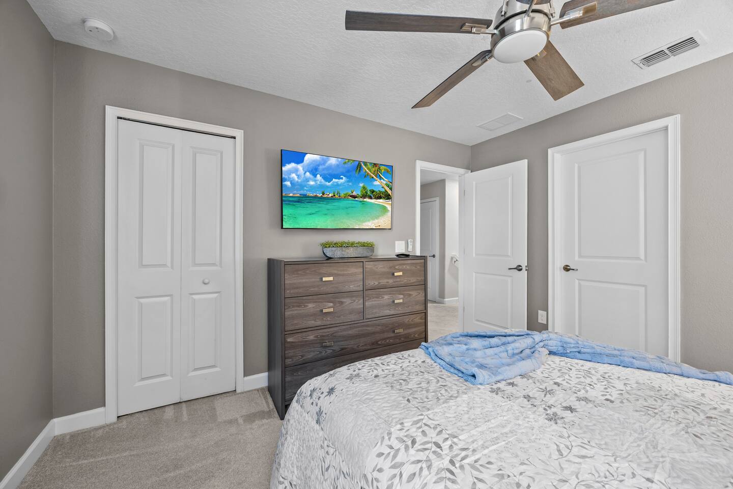 Same bedroom's dresser wall with beach-scene TV and closet