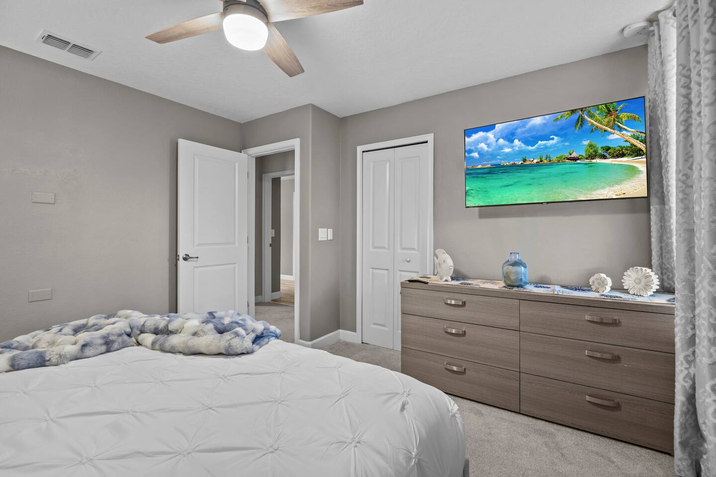 Same bedroom showing gray dresser, wall-mounted TV, and faux-fur throw