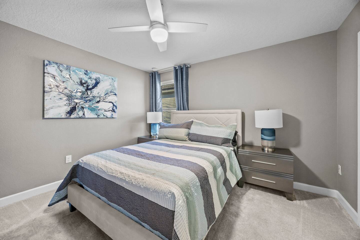 Queen bedroom with diamond-stitched headboard and blue striped quilt