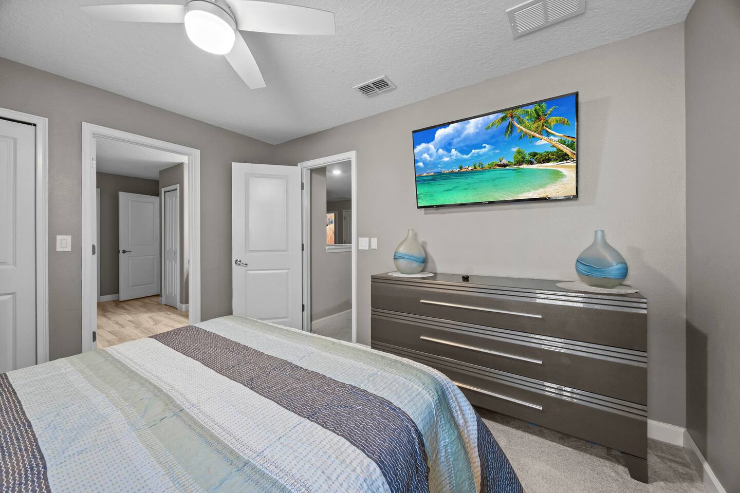 Same bedroom's striped dresser with art-glass vases and wall-mounted TV