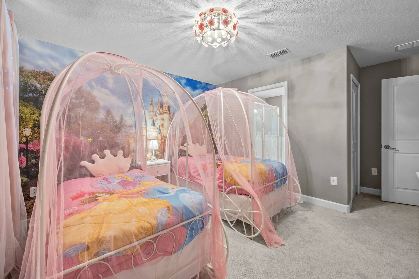 Princess room with two pink-canopy carriage twin beds and floral chandelier