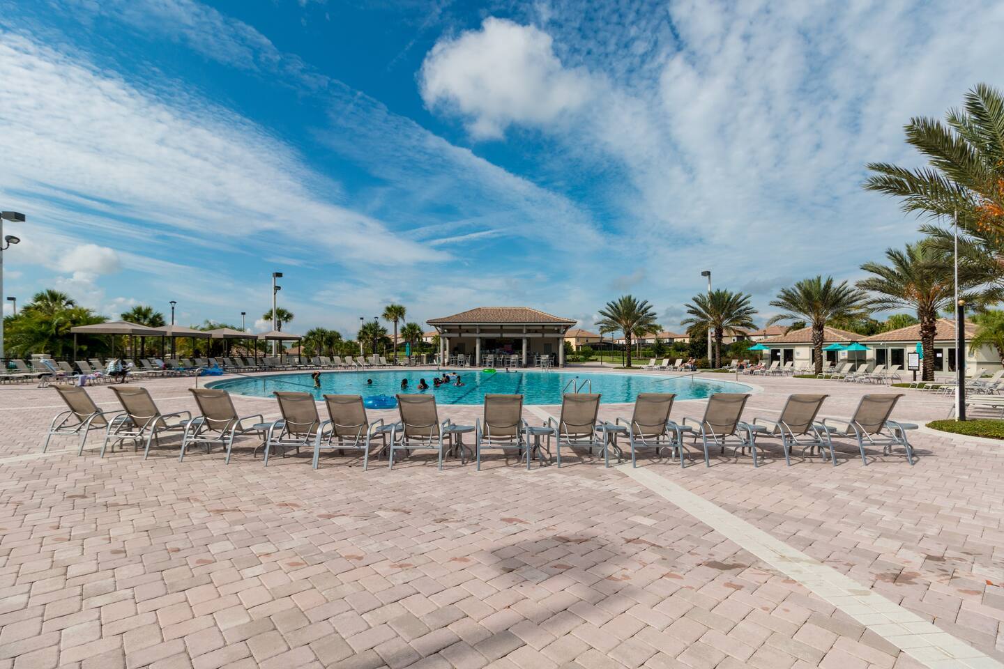 Resort community pool with rows of loungers and clubhouse cabana
