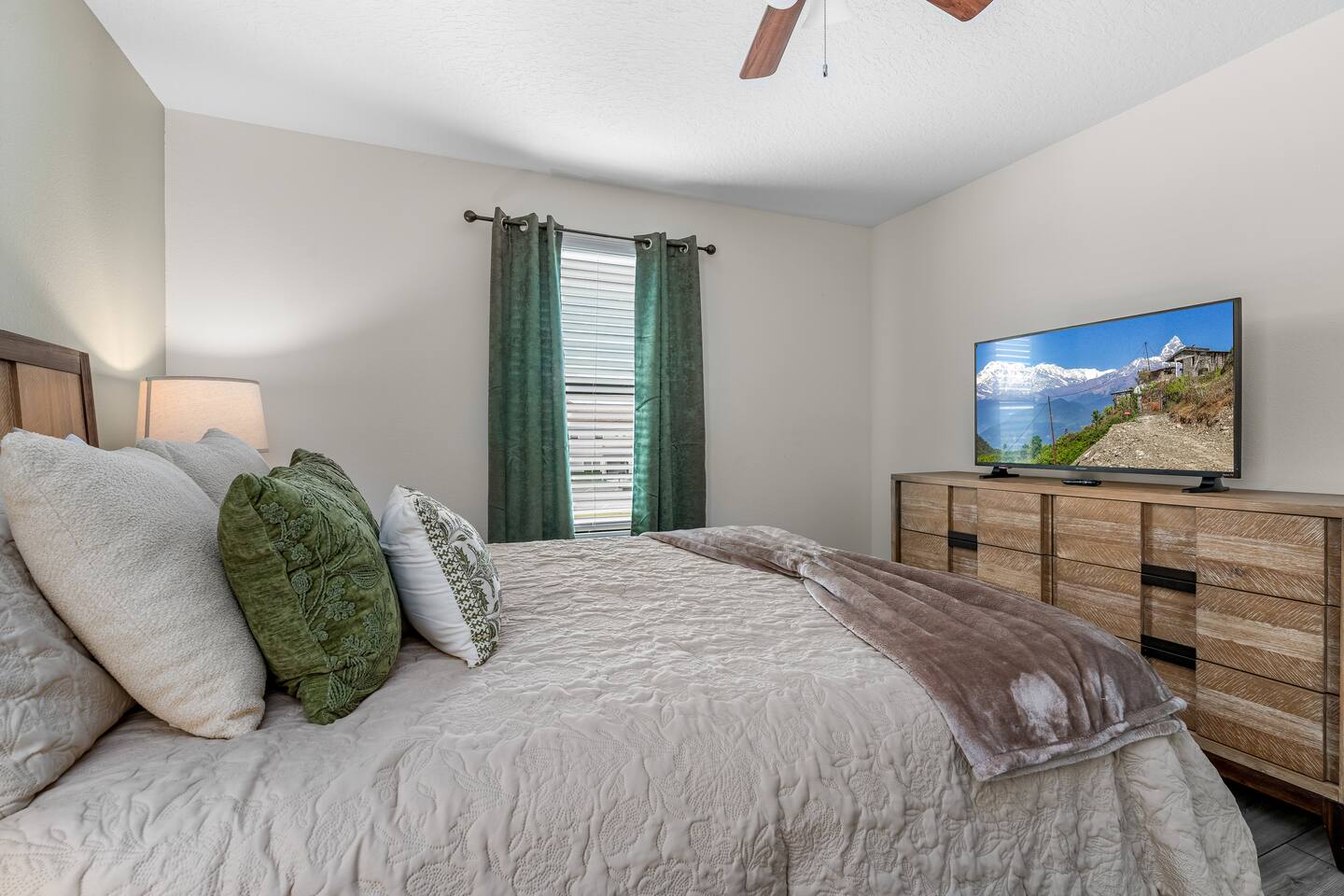 Queen bedroom with green accents, wood dresser, and TV