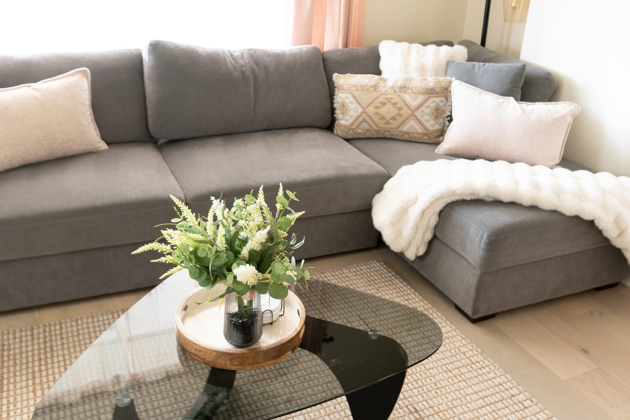 Sunny lounge with plush sectional, soft throws, and a sleek glass table.