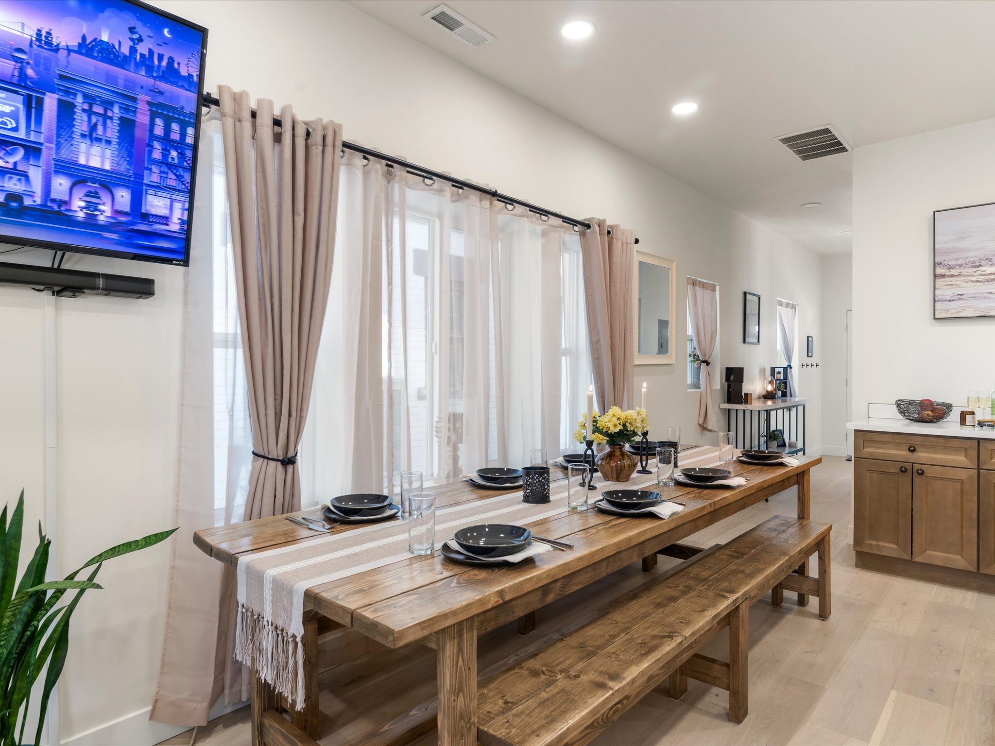 Long farmhouse dining table set for a group beside the wall-mounted smart TV