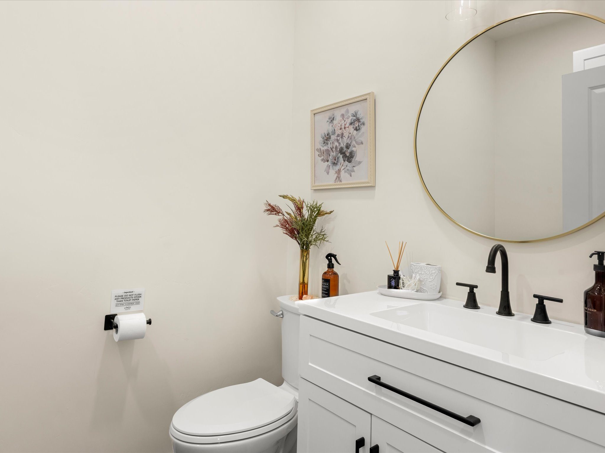 Half bath with a round gold-framed mirror and white floating vanity