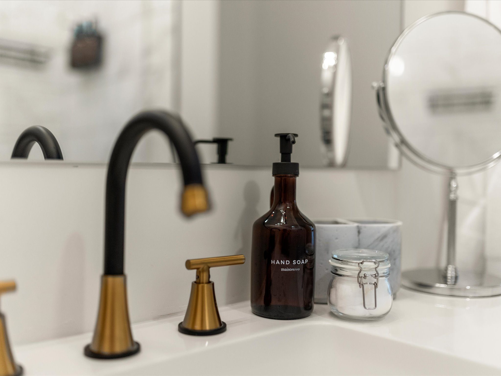 Vanity with a matte-black and gold faucet and magnifying mirror