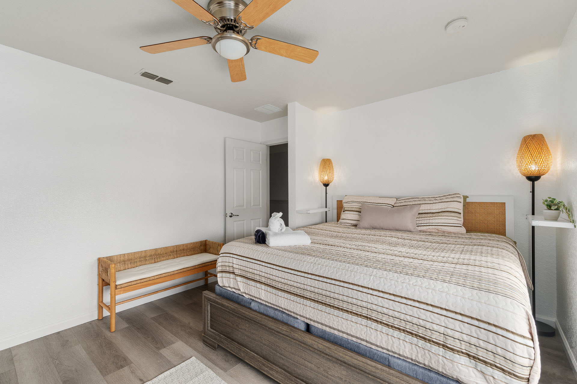 King bedroom with rattan headboard, reading lamps, and a woven bench.