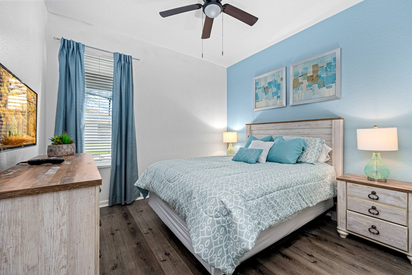 Queen bedroom in calming blues with dresser, TV, and bedside lamps.