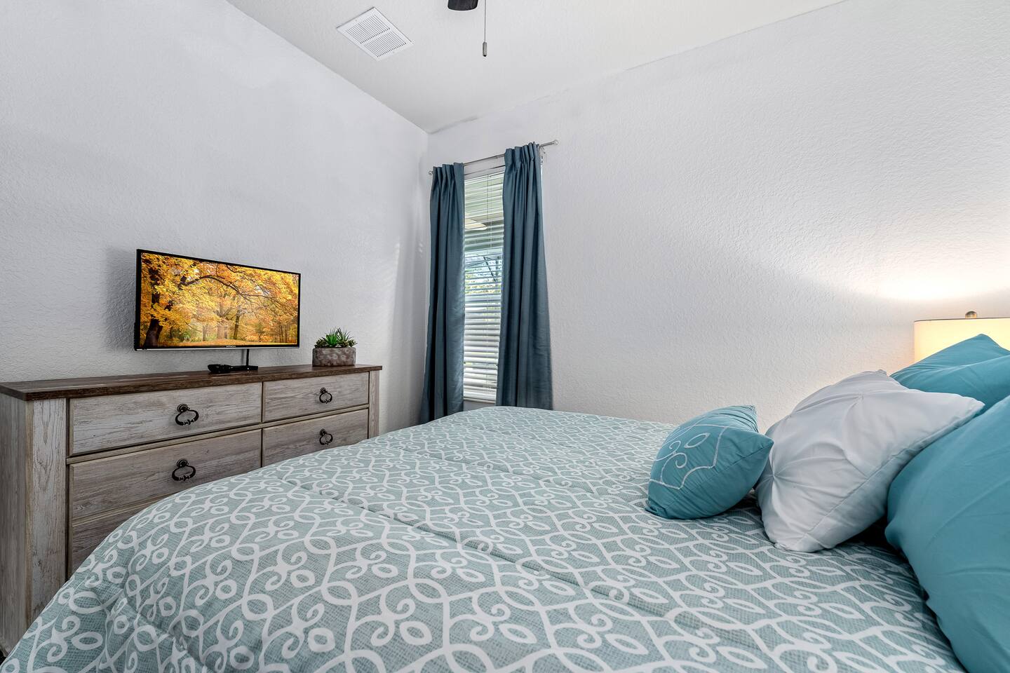 Queen bedroom with wall-mounted TV and blackout curtains.
