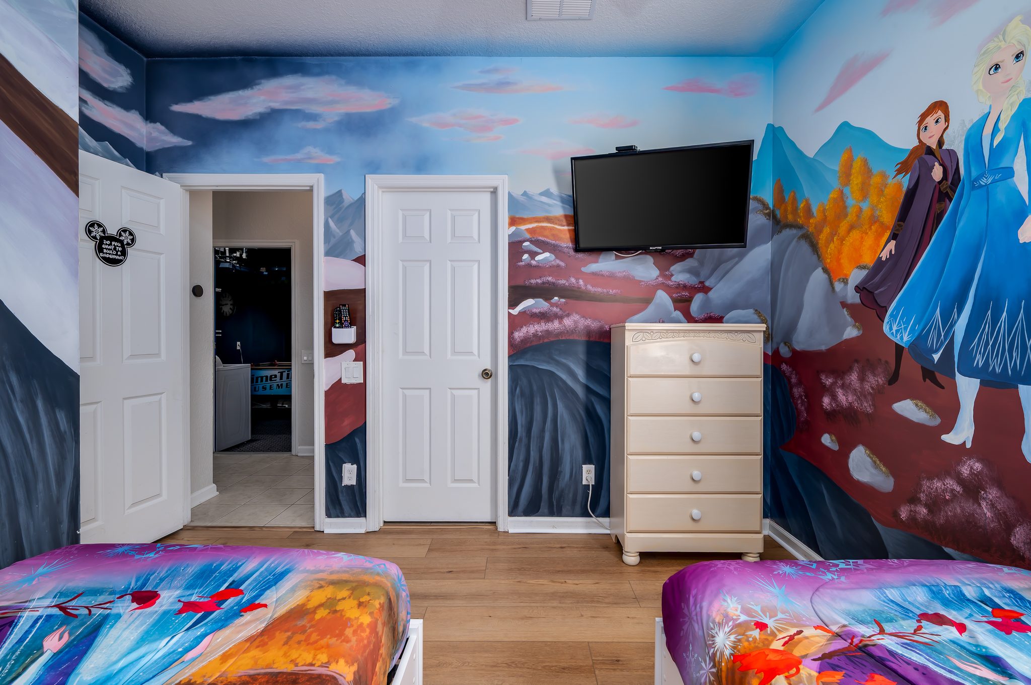 Whimsical Frozen-themed kids’ room with twin beds, mural and TV