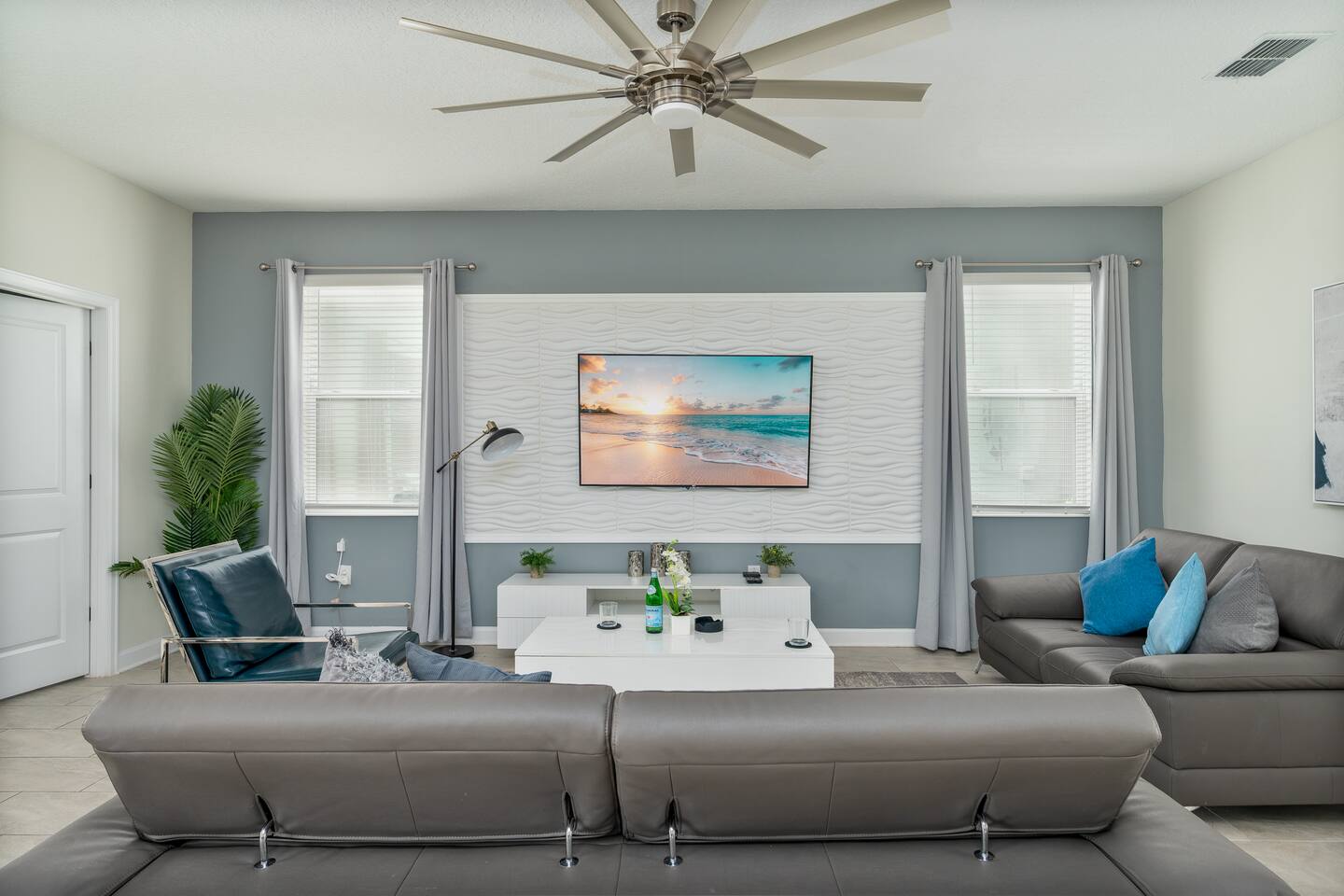 Living room with leather sofas, ceiling fan, and TV on a textured accent wall