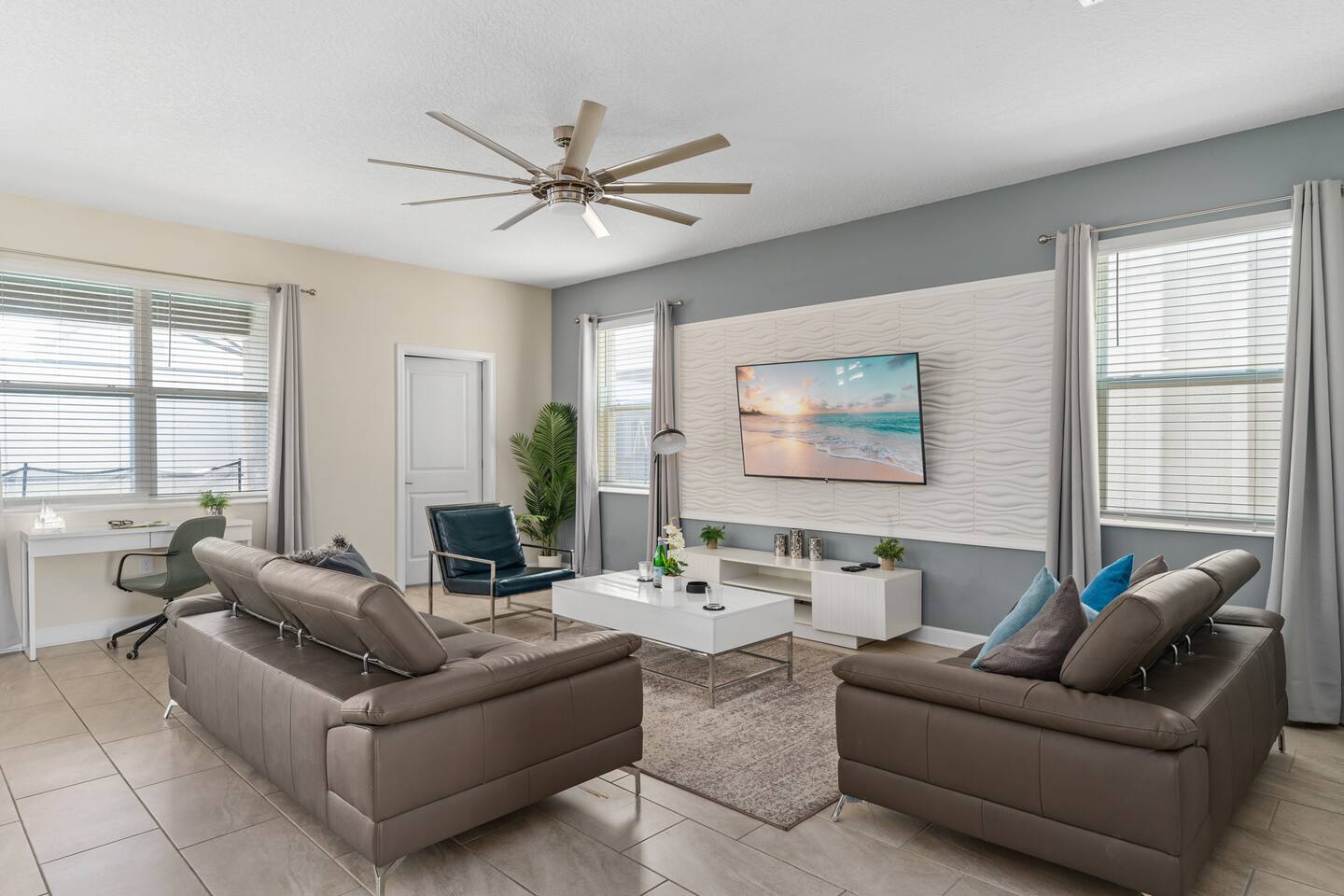 Living area with dual sofas, accent chair, desk nook, and wall-mounted TV