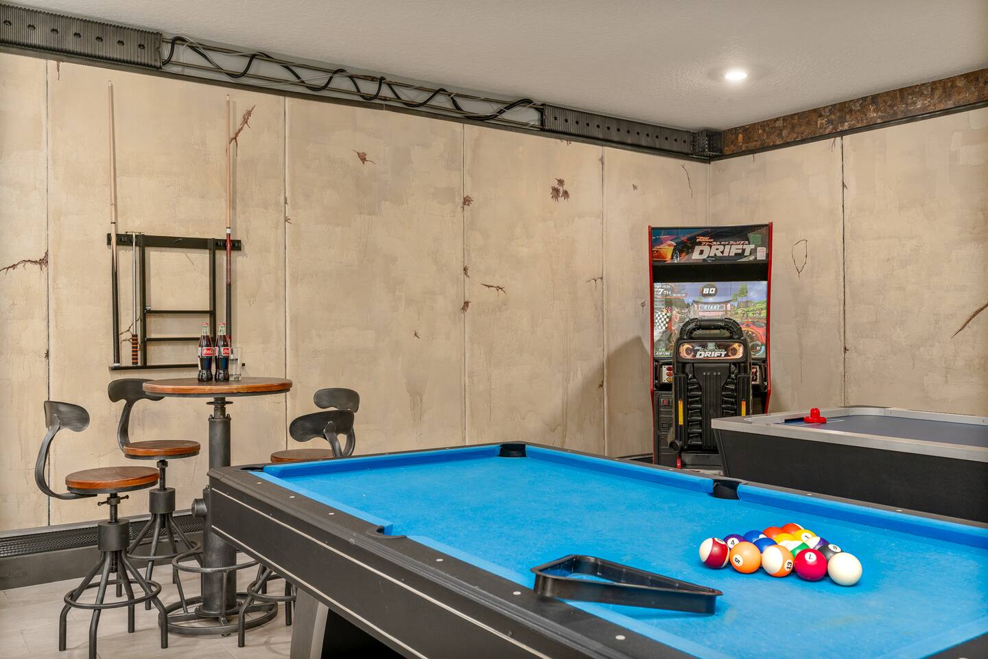 Pool table racked and ready beside the racing arcade game and pub table