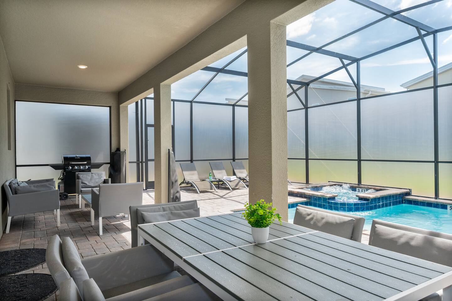 Covered lanai with outdoor dining table, lounge seating, and BBQ grill beside th