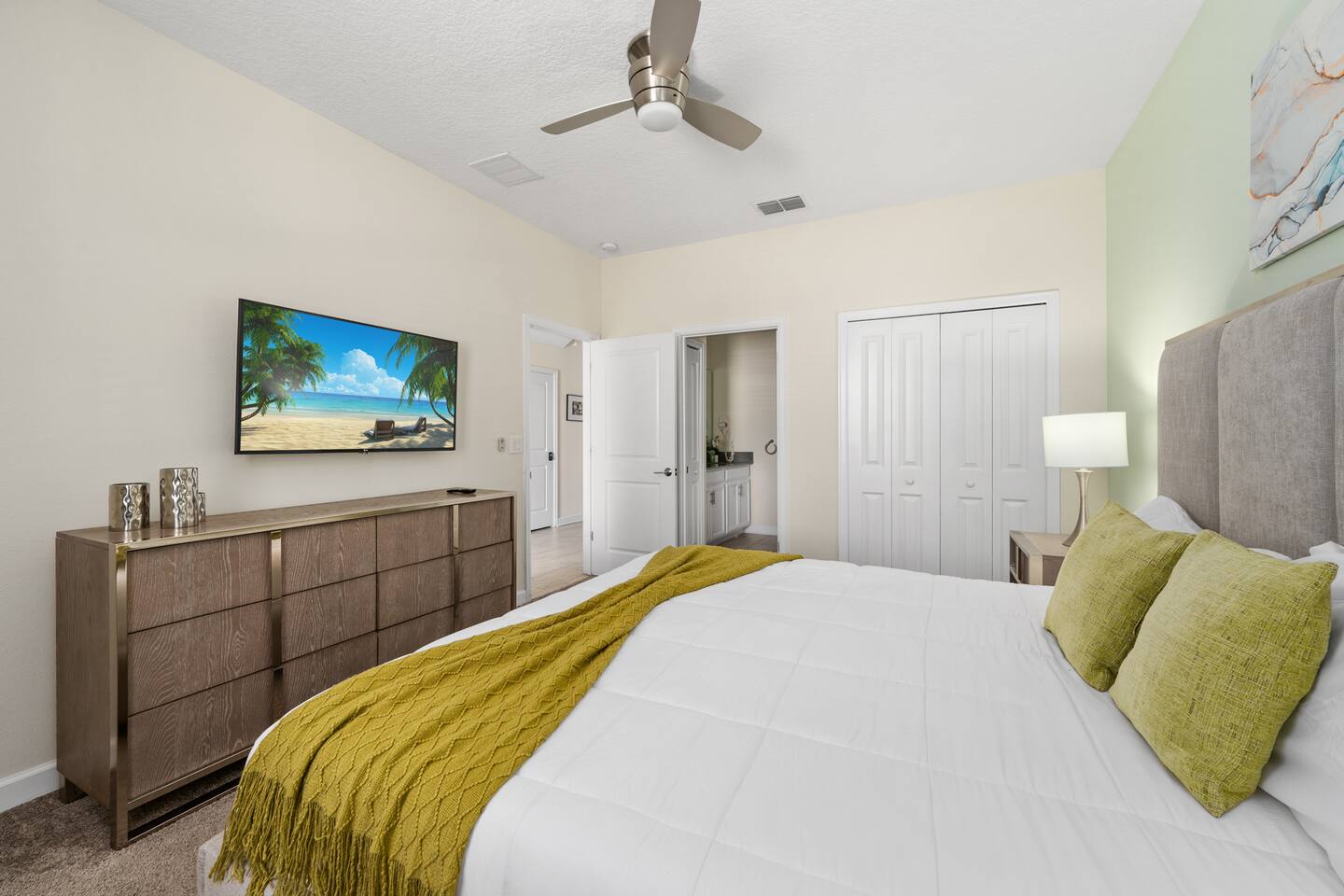 King bedroom with green accent wall, wall-mounted TV, and en suite bath