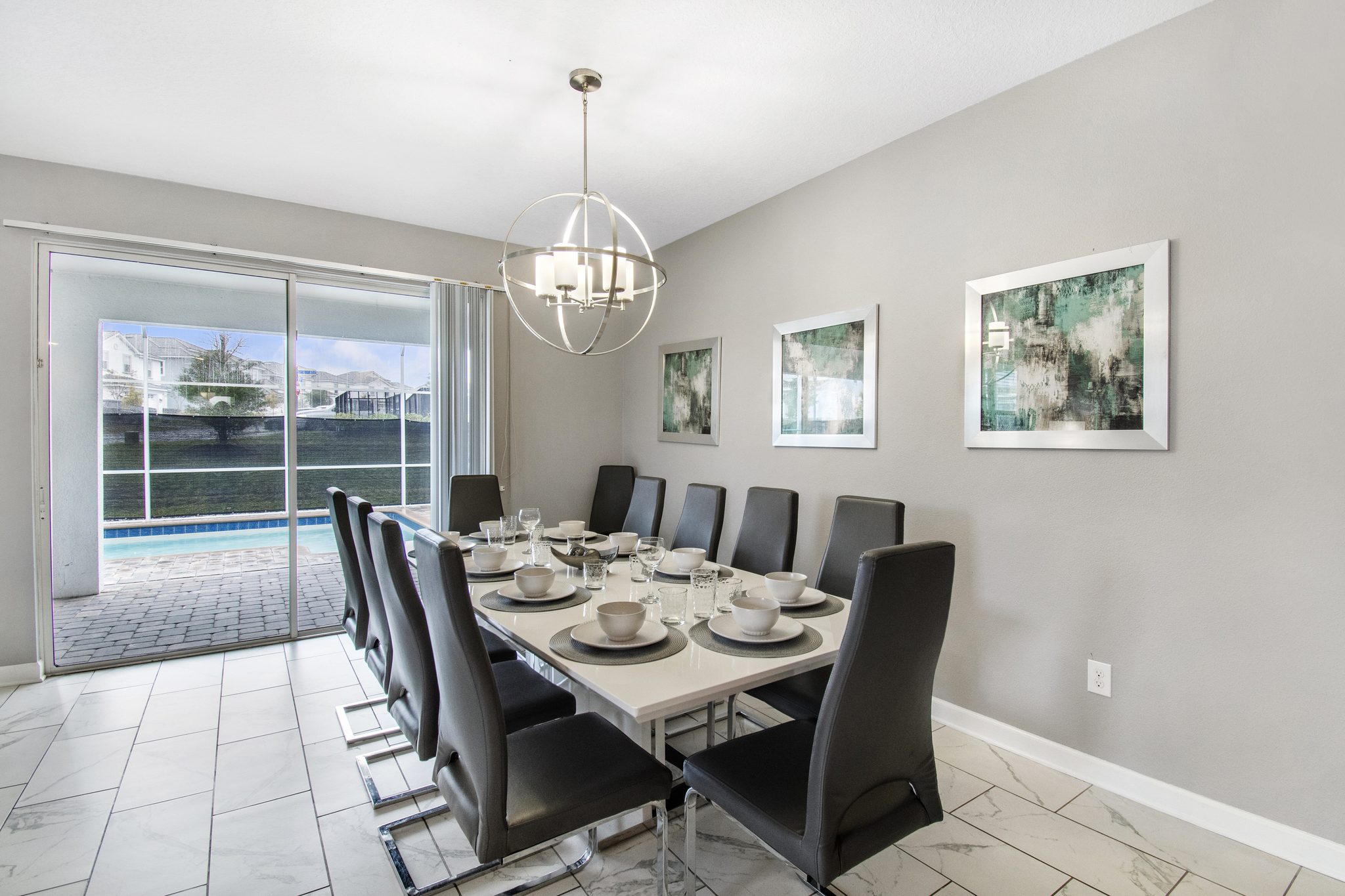 Dining room seating ten with a globe chandelier and sliding doors to the pool de
