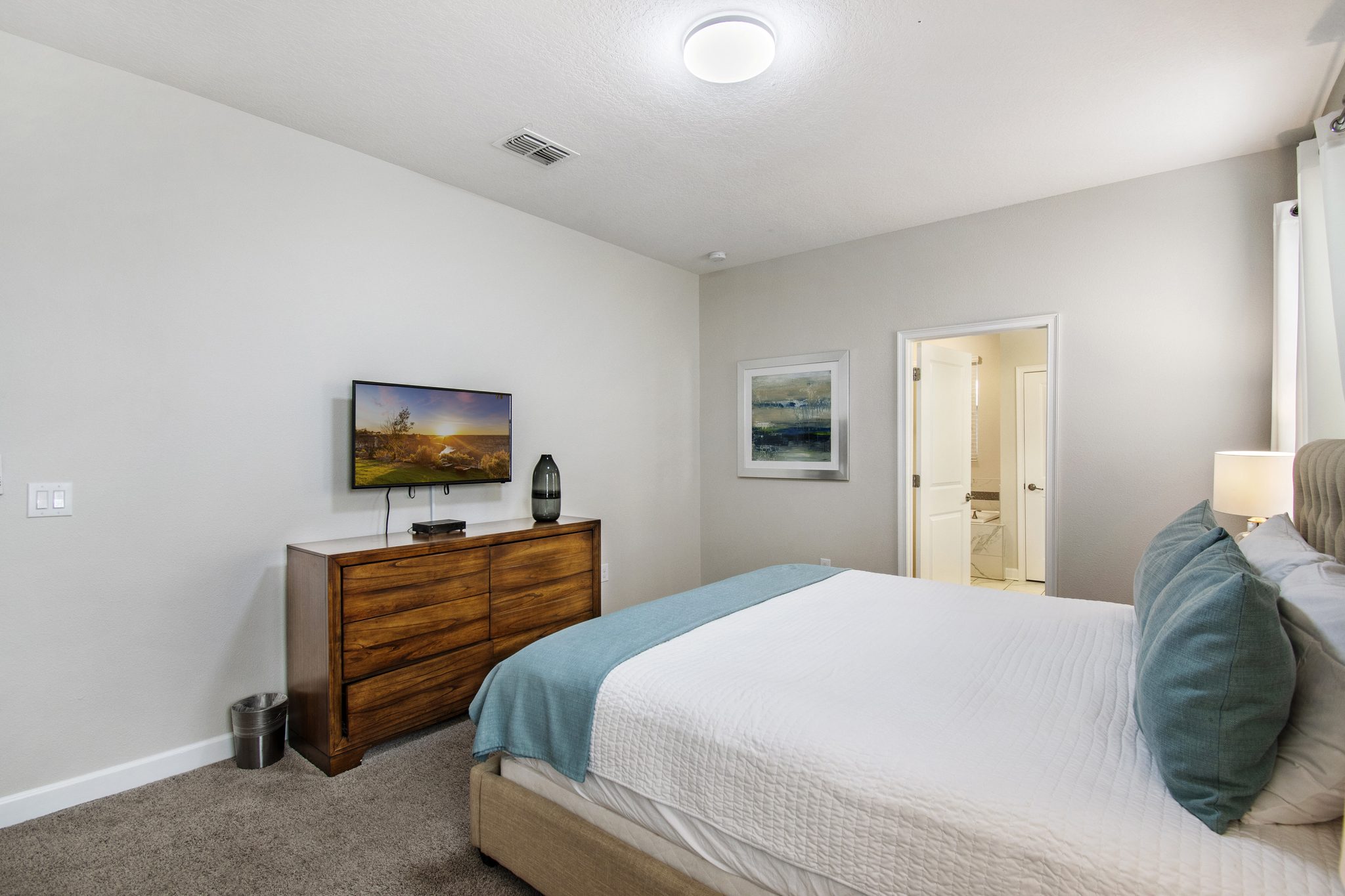 Bedroom with a queen bed, wood dresser, wall-mounted TV, and en-suite bathroom